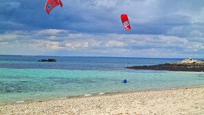 Una playa con agua turquesa cristalina, costa rocosa y una persona en el agua.