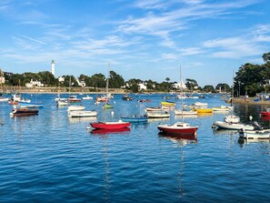 A marina with various boats docked, calm water, and a lighthouse in the background.