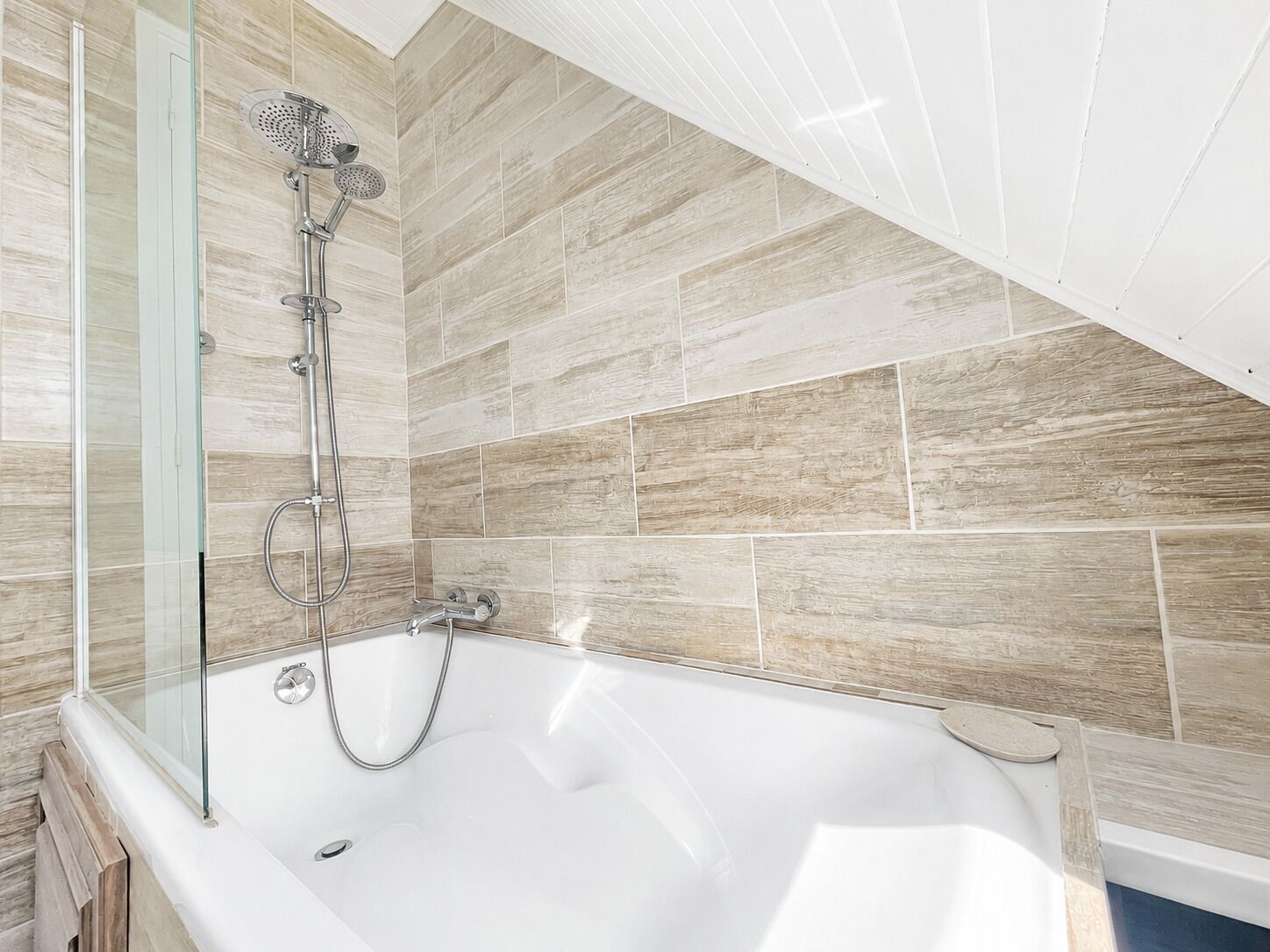 Une salle de bain moderne avec une baignoire sur pieds, un espace de douche fermé par des parois de verre et un mur recouvert de carreaux imitant le motif du bois.