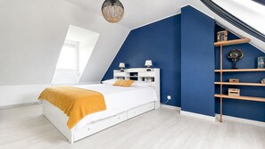 A bedroom with a white bed, a blue accent wall, a wooden shelf, and a skylight. - Élégante et cosy, maison classée 3*, à quelques pas de la plage du Teven (Île-Tudy)