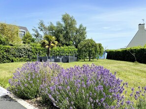 Un barrio residencial con césped, arbustos de lavanda y un edificio moderno con techo inclinado.