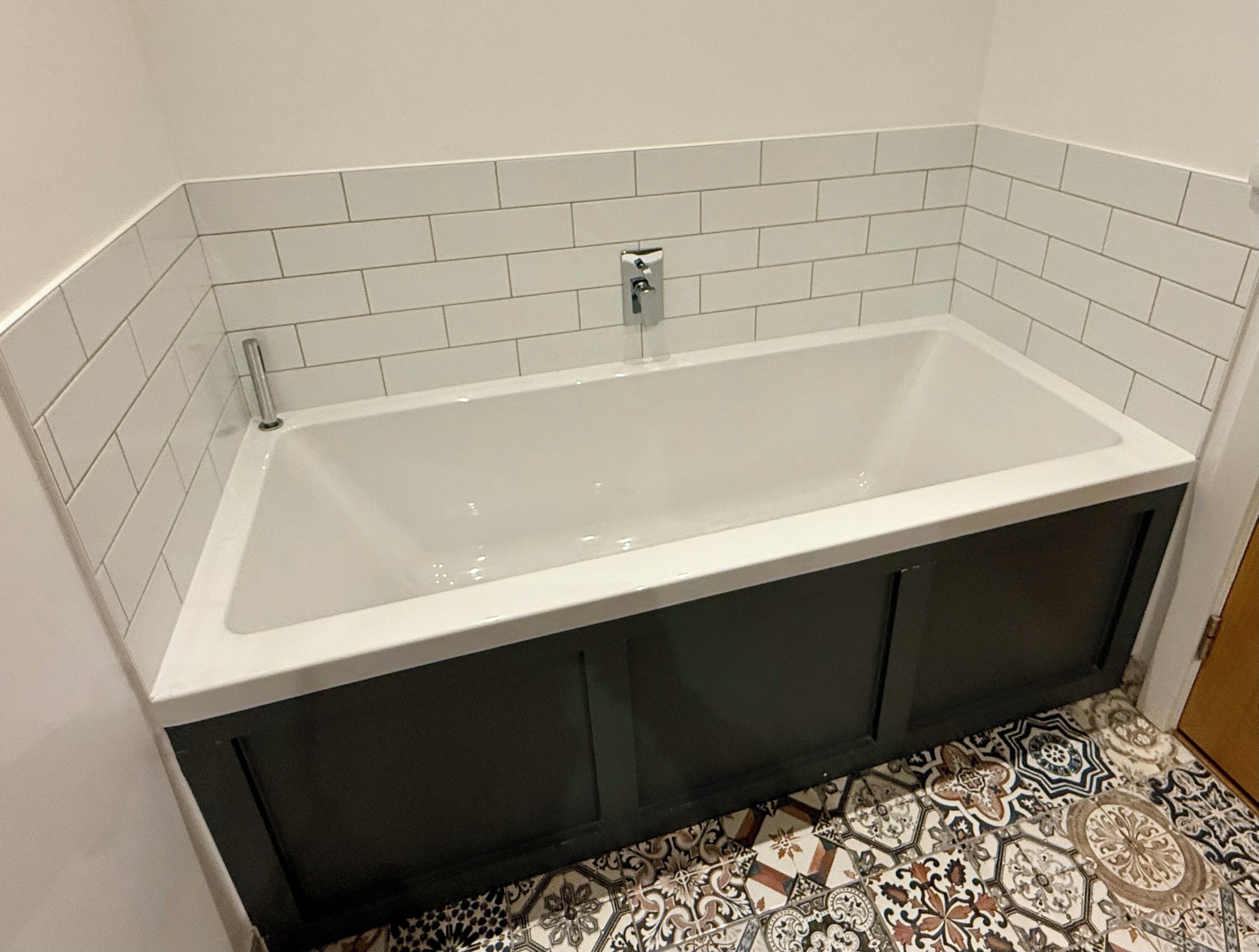 A modern bathroom with a rectangular bathtub, white tiled walls, and a patterned floor.