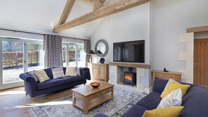 Ein Wohnzimmer mit Sofa, Couchtisch, Kamin, Fernseher und großen Fenstern.