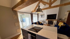 Eine moderne Küche mit einer großen Kochinsel, Holzbalken, einem Essbereich mit blauem Sofa und einem Fernseher über einem Kamin.