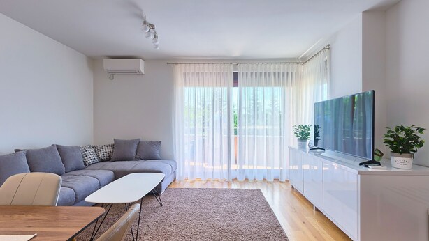 A modern living room with a grey sofa, a wooden coffee table, a TV on a white cabinet, and sheer curtains. - Maris apartment (Ližnjan)