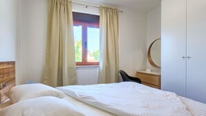 A bedroom with a bed, a chair, a dresser, a mirror, and a window with curtains. - Maris apartment (Ližnjan)