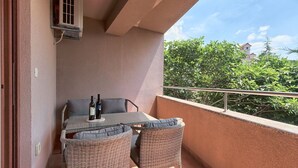 A balcony with a table and chairs, two bottles of wine, and a view of greenery and buildings. - Maris apartment (Ližnjan)