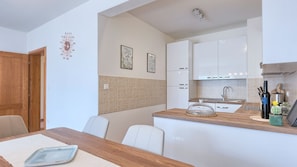 A compact kitchen with white cabinets, a tiled backsplash, and a wooden dining table with chairs.