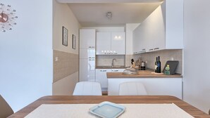 A modern kitchen with white cabinets, a wooden countertop, and a dining area with a table and chairs. - Maris apartment (Ližnjan)