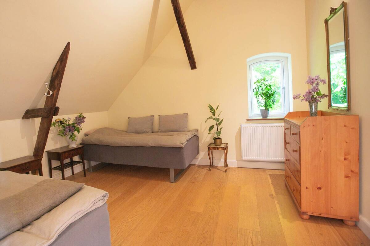 A cozy attic bedroom with a sloped ceiling, a bed, a dresser, and a window with plants.