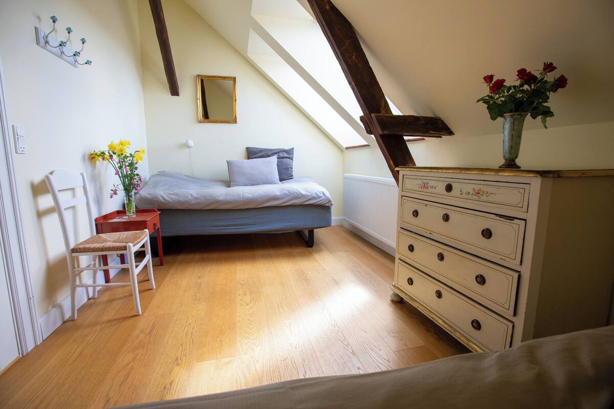 A bedroom with a bed, dresser, chair, and a skylight.