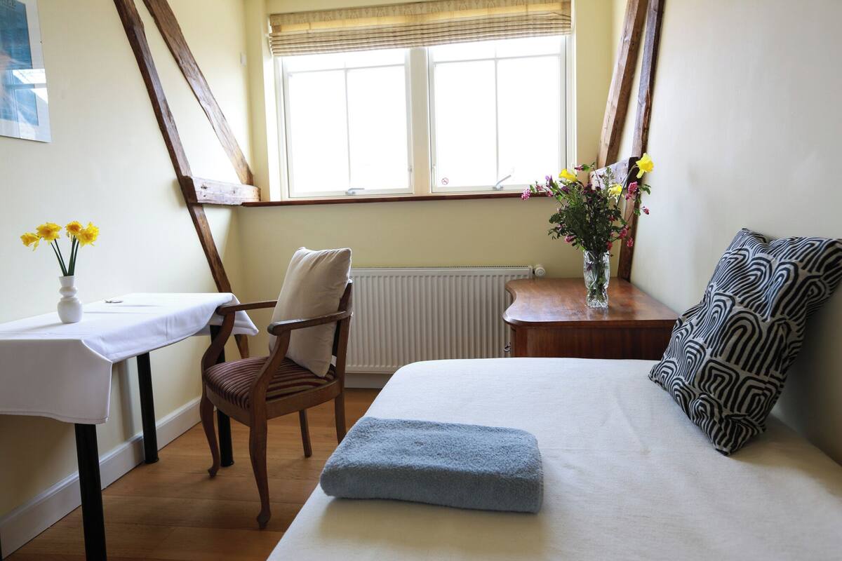 A bedroom with a bed, a chair, a small table, and a window with curtains.