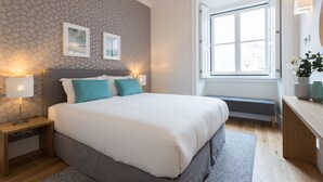 Un dormitorio ordenado con una cama grande, lámparas de noche, un banco y una ventana con vistas.