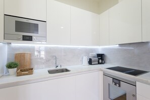 Une cuisine moderne avec des meubles blancs, un four à micro-ondes encastré, un évier et une machine à café.