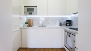 Una cocina moderna con armarios blancos, microondas integrado, cafetera y tabla de cortar de madera.