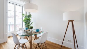 Un comedor moderno con una mesa de vidrio, sillas blancas, una planta en maceta y una lámpara de pie.