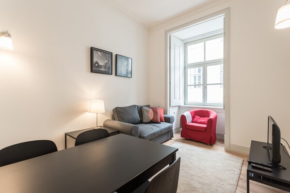 A modern living room with a dining table, a sofa, a red armchair, and a TV on a stand.