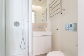 Um banheiro moderno com box de vidro, pia branca com bancada de mármore e porta-toalhas na parede.