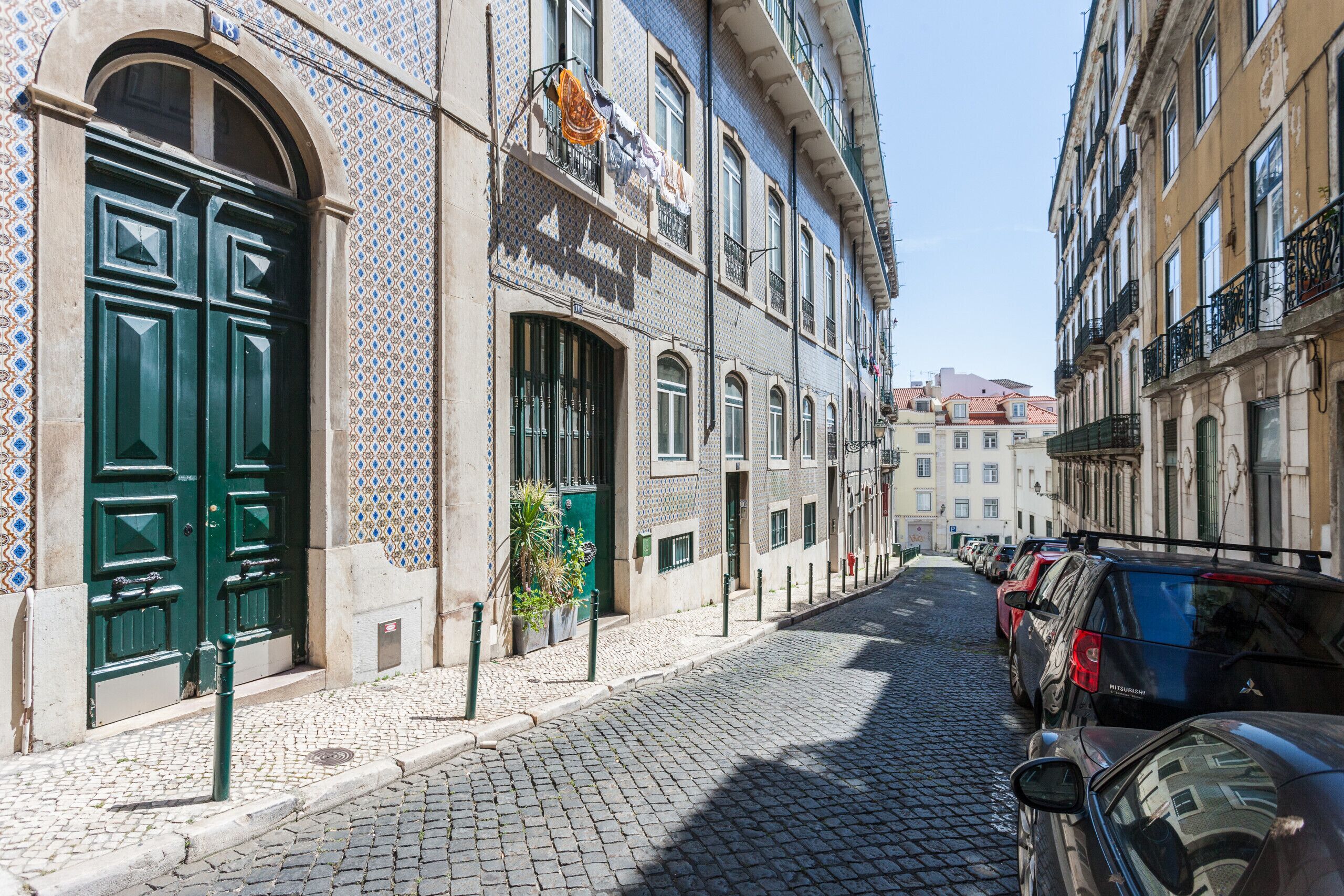 Une rue pavée bordée de bâtiments historiques aux façades carrelées et aux portes vertes à double battant.
