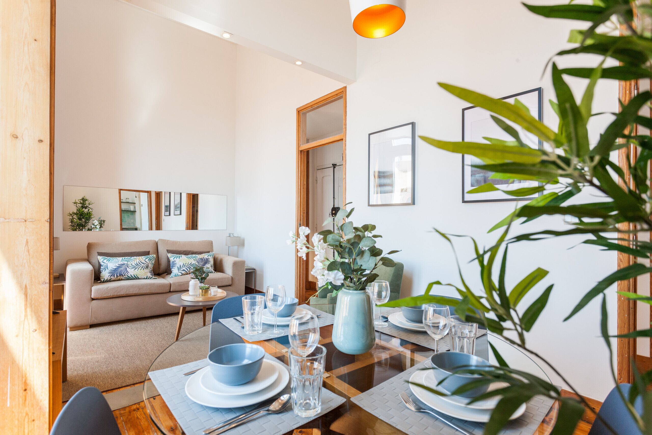 Una sala de estar moderna con un sofá, una mesa de comedor preparada para cuatro personas y un ventanal grande.