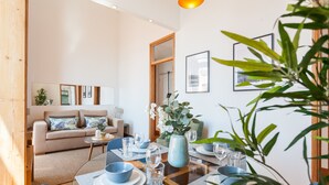 A modern living room with a sofa, dining table set for four, and a large window. - FLH Alfama River View Flat (Lisbon)