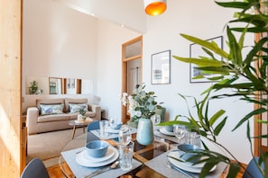 Ein modernes Wohnzimmer mit Sofa, Esstisch für vier Personen und einem großen Fenster.