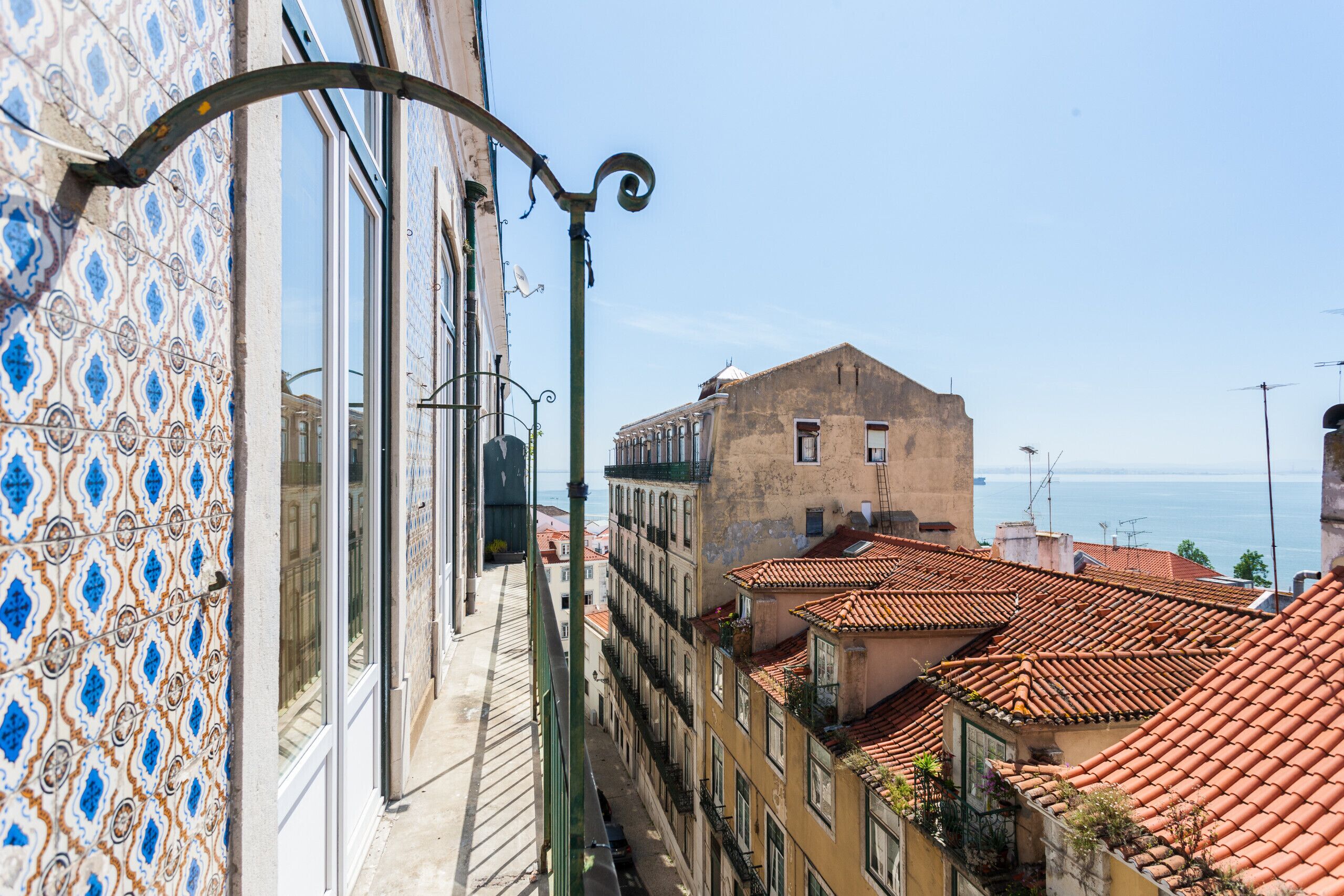 Une rue étroite bordée d’immeubles aux façades décorées de carreaux bleus et blancs, avec vue sur la mer, et un bâtiment surmonté d’un toit recouvert de tuiles rouges.