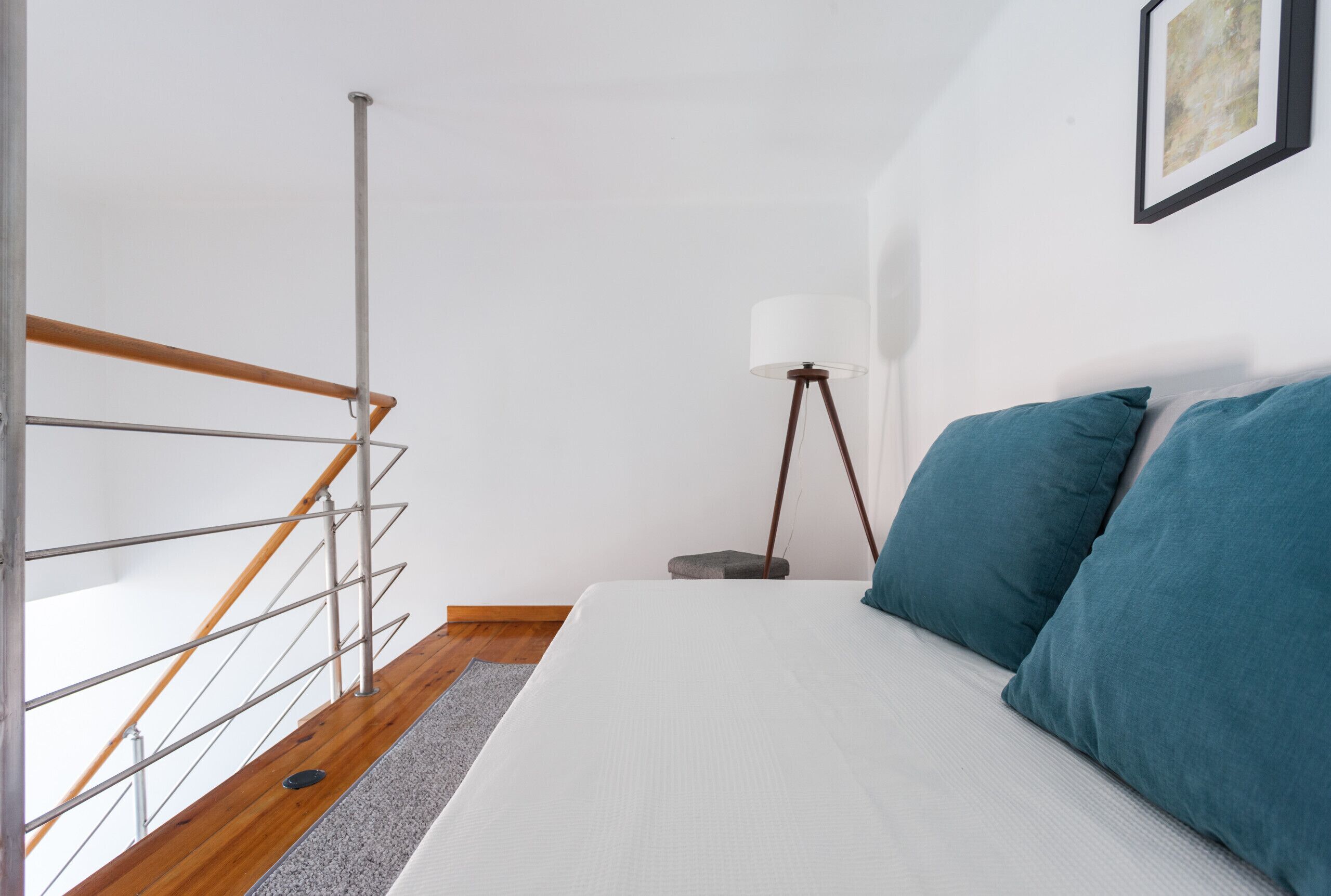 Ein Schlafzimmer mit einem Bett, blauen Kissen, einer Stehlampe und einer Treppe.