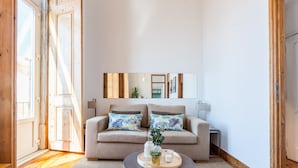 A living room with a beige sofa, two patterned pillows, a round coffee table with a tray, a small plant, and a white lamp. - FLH Alfama River View Flat (Lisbon)