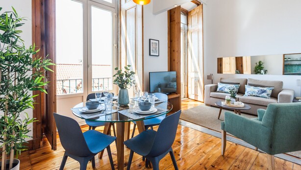 A modern living room with a glass dining table, two blue chairs, a sofa, and a TV. - FLH Alfama River View Flat (Lisbon)