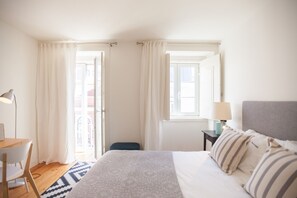 A hotel room with a bed, a desk, a chair, a lamp, and a view through the open door. - FLH Príncipe Real with View (Lisbon)
