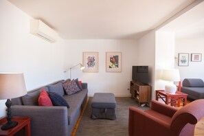 A modern living room with a grey sofa, a red armchair, a small ottoman, a TV, and a wooden cabinet. - FLH Príncipe Real with View (Lisbon)