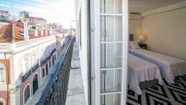 A hotel room with a balcony overlooking a cityscape, featuring a bed, a nightstand, and a view of buildings. - FLH Príncipe Real with View (Lisbon)