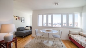 A modern living room with a round table, grey sofa, and a large window with a city view. - FLH Príncipe Real with View (Lisbon)
