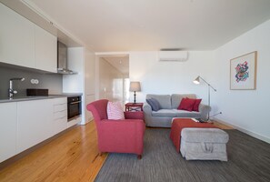 A modern apartment with a kitchen, a grey sofa, a red armchair, and a grey ottoman.