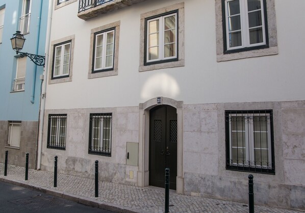 Un bâtiment doté d’une grande porte sombre, de nombreuses fenêtres avec des barreaux en métal et situé sur une rue pavée.