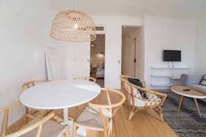 Un salon moderne avec une table à manger ronde, des chaises en osier, un téléviseur à écran plat fixé au mur et un tapis à motifs sur le sol.