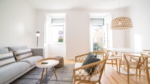 Ein modernes Wohnzimmer mit Sofa, rundem Couchtisch, Korbstühlen und einem Esstisch.