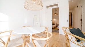Ein Zimmer mit einem runden weißen Tisch, Holzstühlen, einer Korbschaukel und einer gewebten Deckenleuchte.