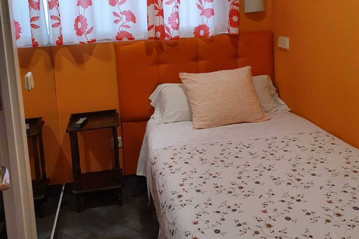 Quarto com cama, mesa de cabeceira e cortinas florais na janela.