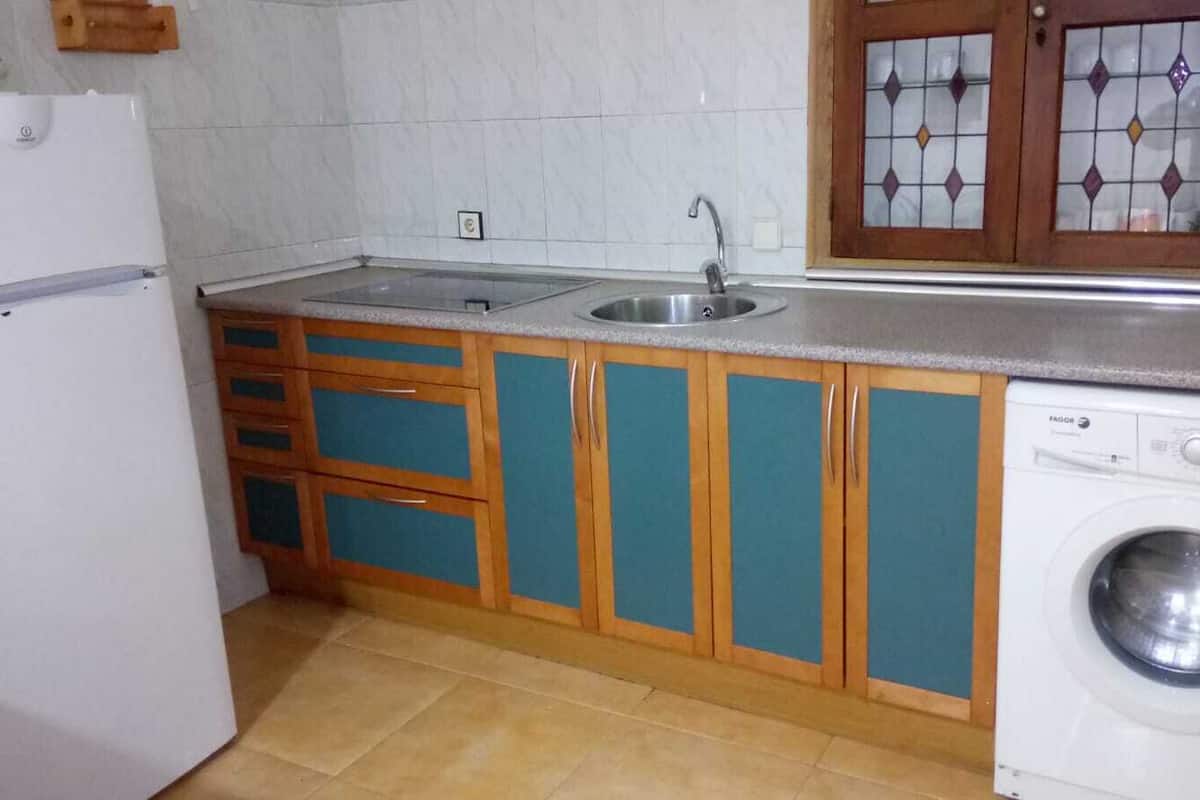 Uma cozinha compacta com pia, armários de madeira, máquina de lavar e geladeira.
