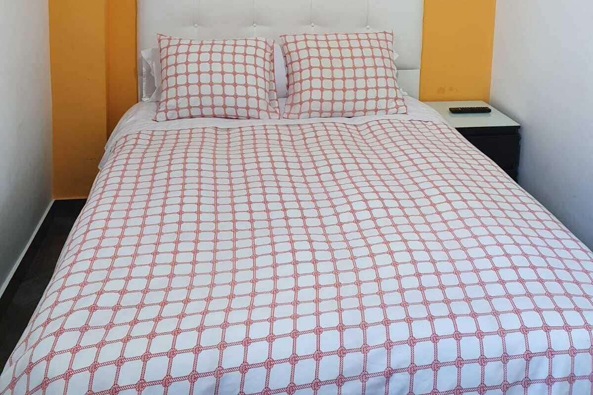 Quarto de hotel com cama, cabeceira, mesa de cabeceira, quadro emoldurado e luminárias fixadas na parede.