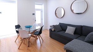 A modern living room with a glass dining table, a dark grey sofa, and two round mirrors on the wall. - FLH Porto Balcony Apartment (Oporto)