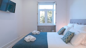 A bedroom with a bed, pillows, a window, and a TV mounted on the wall. - FLH Porto Balcony Apartment (Oporto)