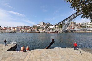 A riverside view with a bridge, boats, and people by the water.
