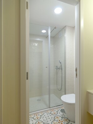 Une douche fermée par des parois de verre, avec des toilettes blanches et des carreaux de sol à motifs.