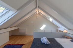 A modern, well-lit attic bedroom with a skylight, a bed with rolled towels, a desk, and a nightstand.