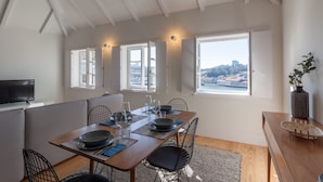 A dining area with a wooden table set for four, a television on the left, and a view of a cityscape through large windows. - FLH Douro View Luxury Duplex (Oporto)