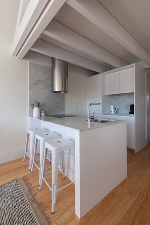 A modern kitchen with a central island, white bar stools, a stainless steel sink, and a marble backsplash.