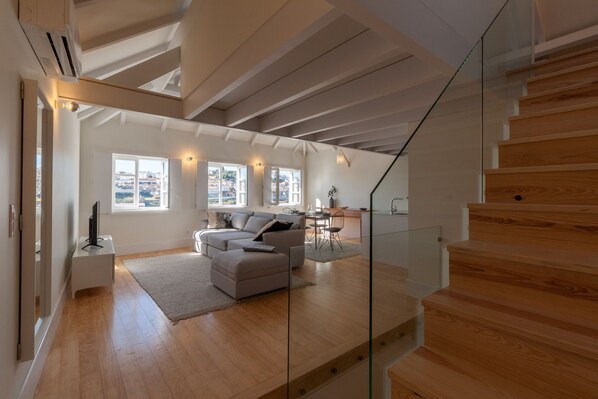 A modern living room with a sofa, a dining area, and a staircase.